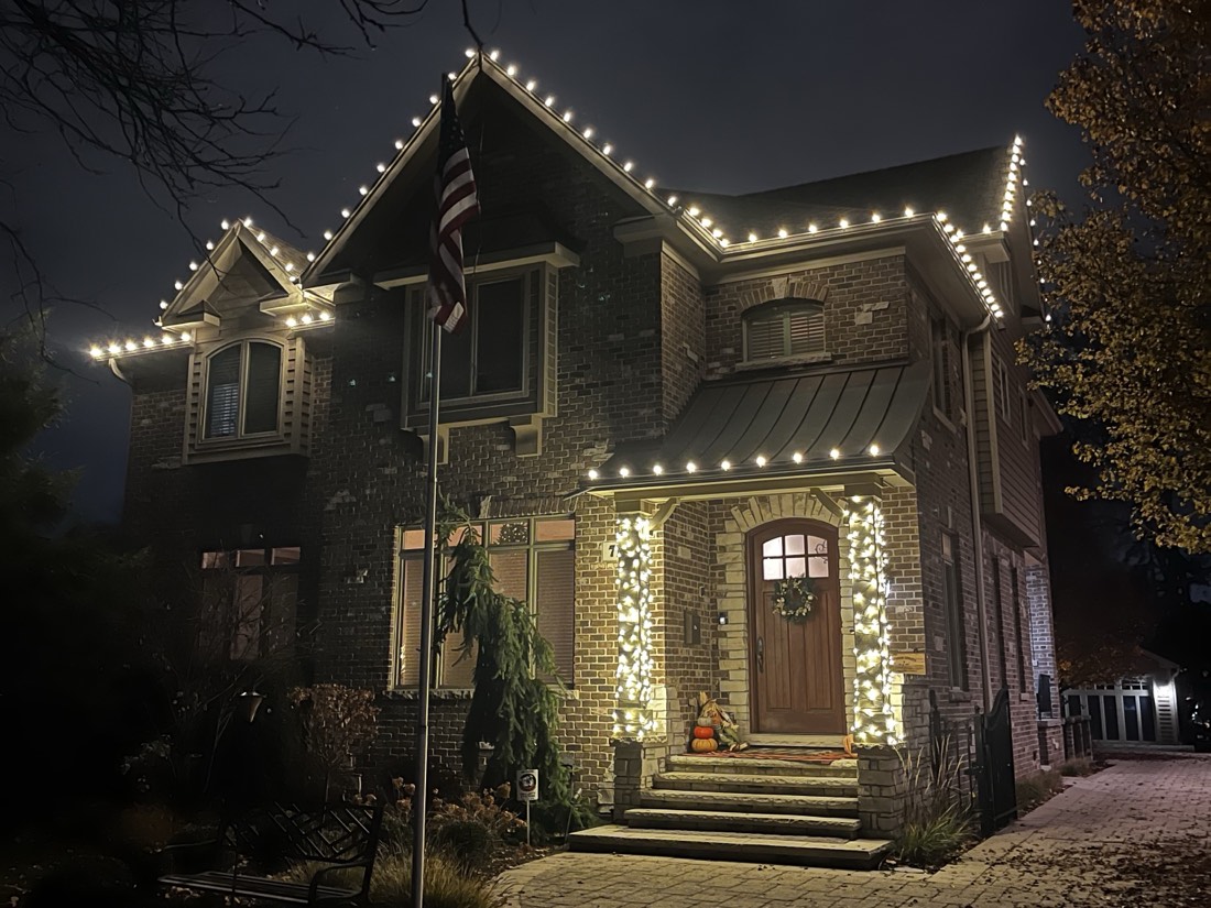 Brick and stone home at blue hour with warm white C9 bulbs on the gables and porch, columns wrapped in mini lights