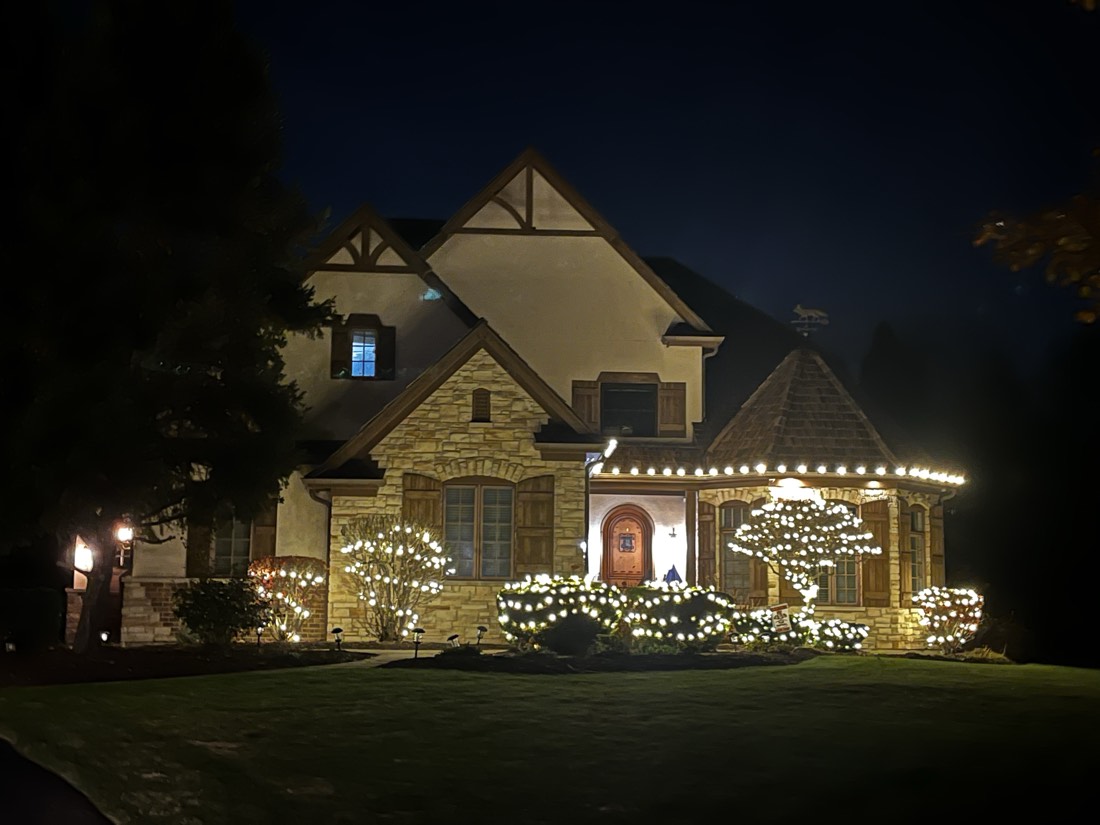 Tudor-style home with a stone turret outlined in warm white C9 bulbs, front hedges and an ornamental tree fully wrapped